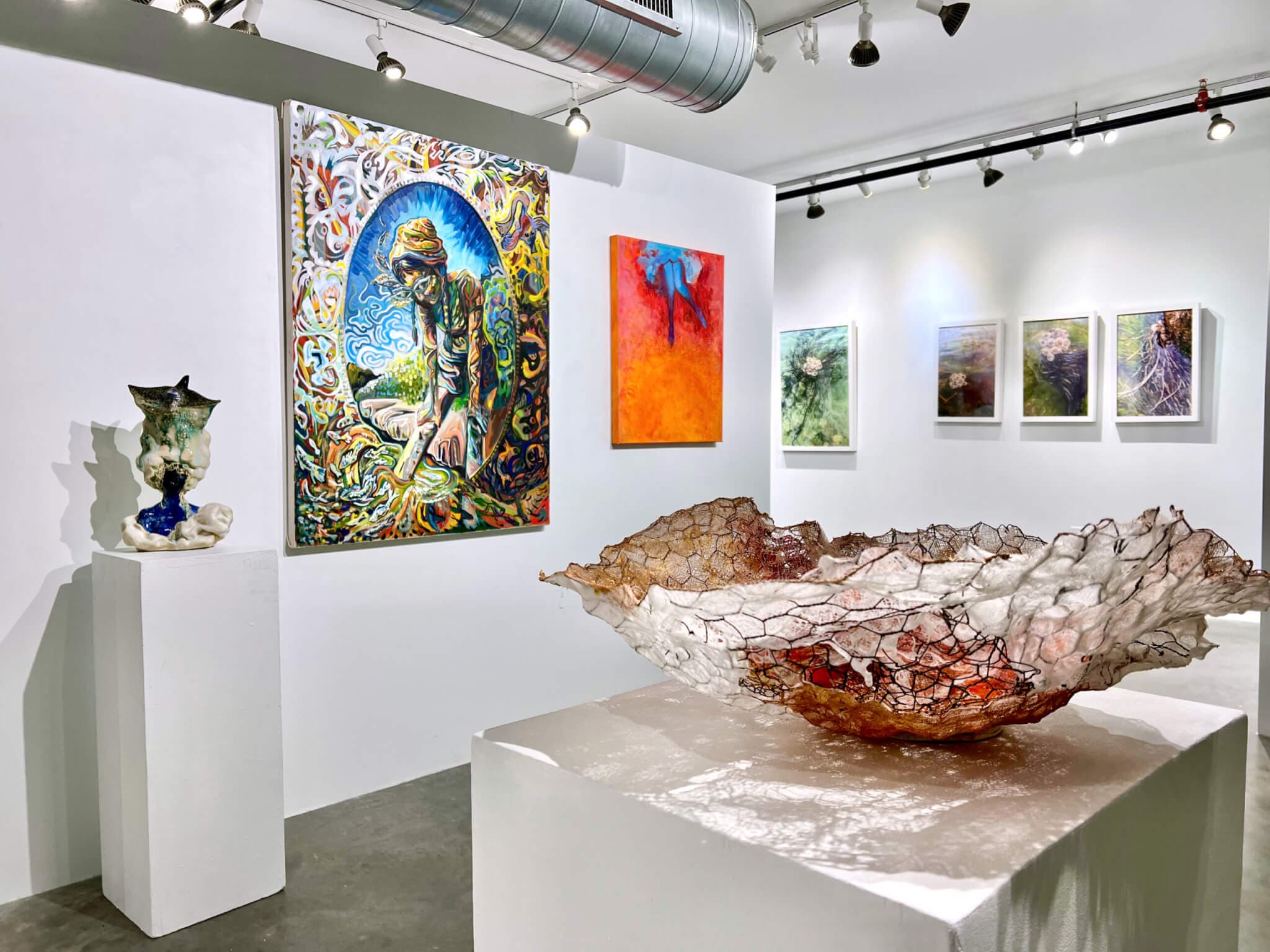 A sculptural vessel sitting on a pedestal foregrounds the image, with six paintings of various sizes and figurative sculpture in the background.
