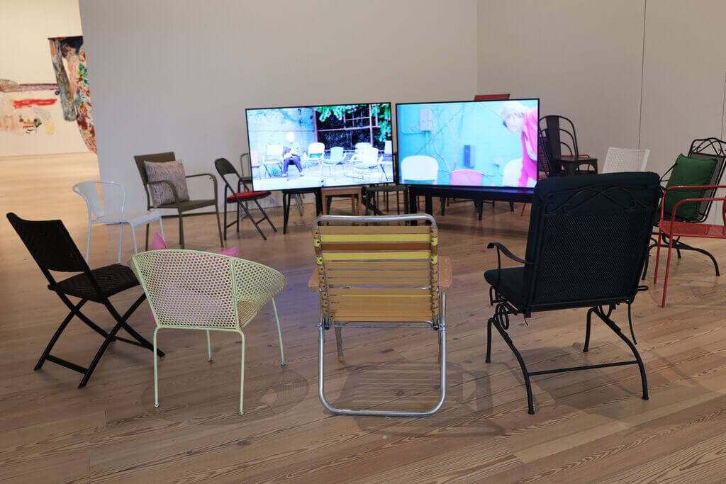Two computer monitors stand surrounded by a circle of various types of chairs.
